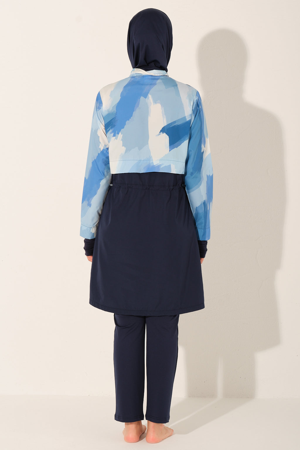 Person wearing a blue and white patterned top with a navy hijab and pants burkini for resort on a light background