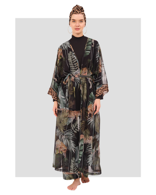 A model wearing a long-sleeve black tunic with a high neckline, wide-leg pants with a jungle-inspired print, a sheer printed kimono, and a leopard-print headscarf.