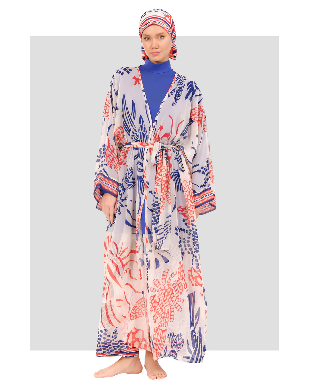 A model wearing a blue, white, and red floral burkini with a high neckline, full sleeves, and a flowing kimono, paired with a matching headscarf.