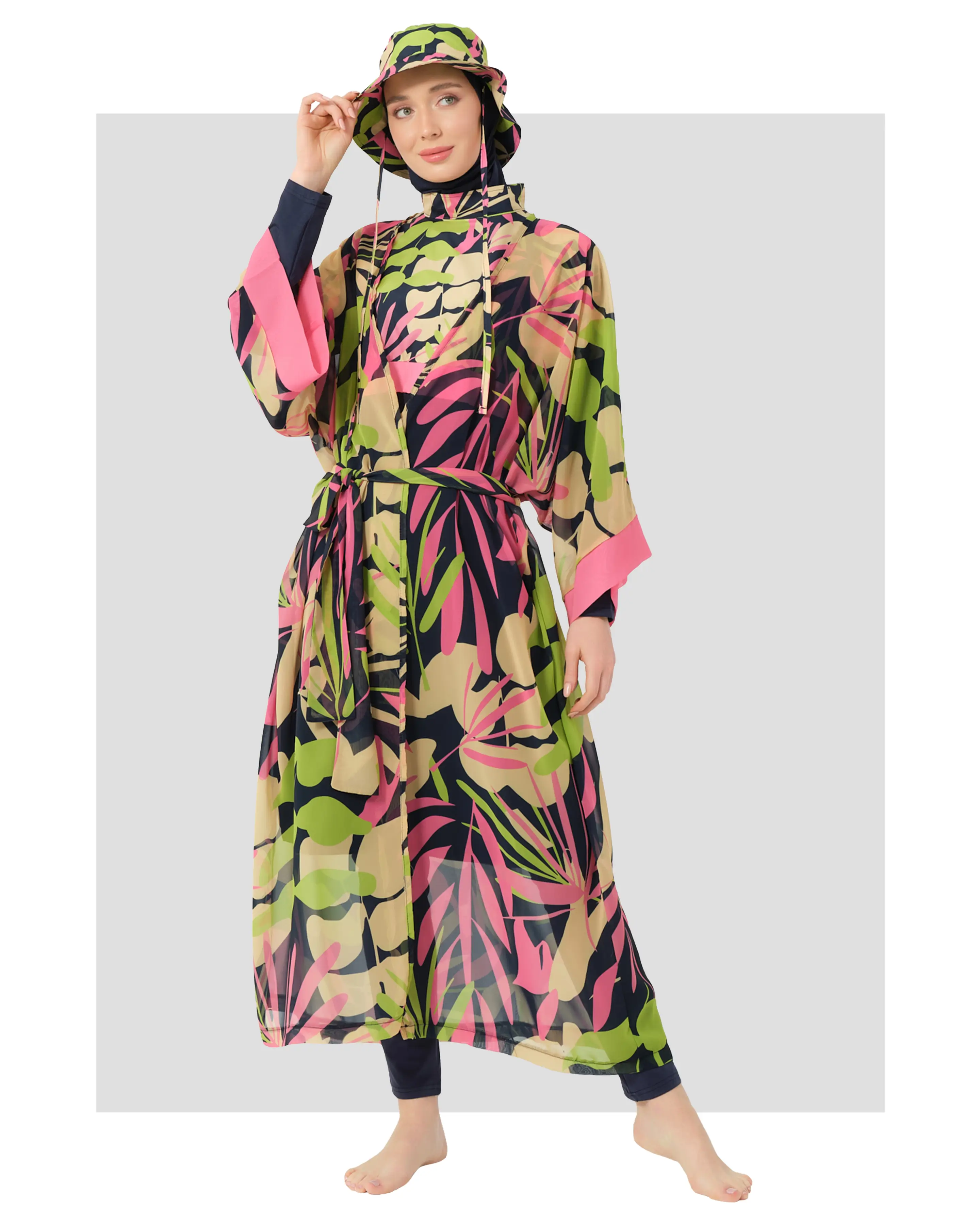 A model wearing a vibrant sheer kimono with a tropical print in shades of pink, green, and navy, accessorized with a matching hat and tie belt.