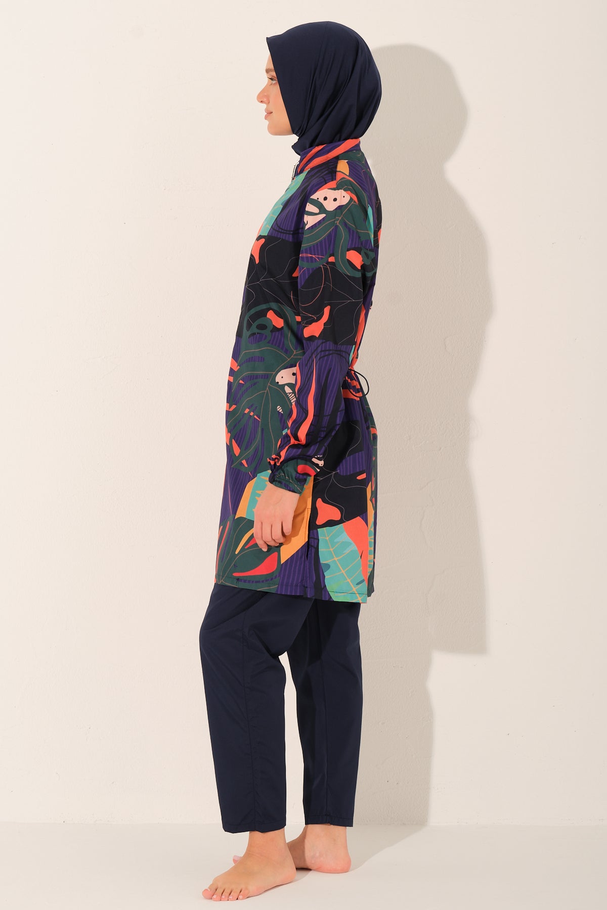 Model in blue tropical print burkini set, profile view, standing calmly.