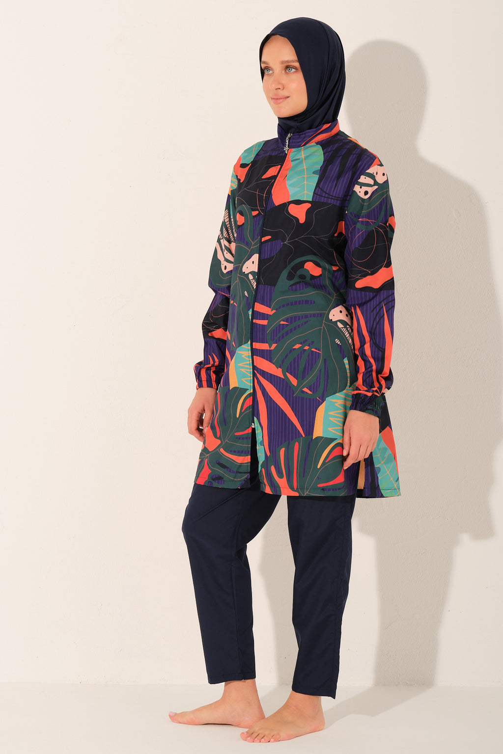 Model in navy tropical print burkini set, profile view, standing calmly.