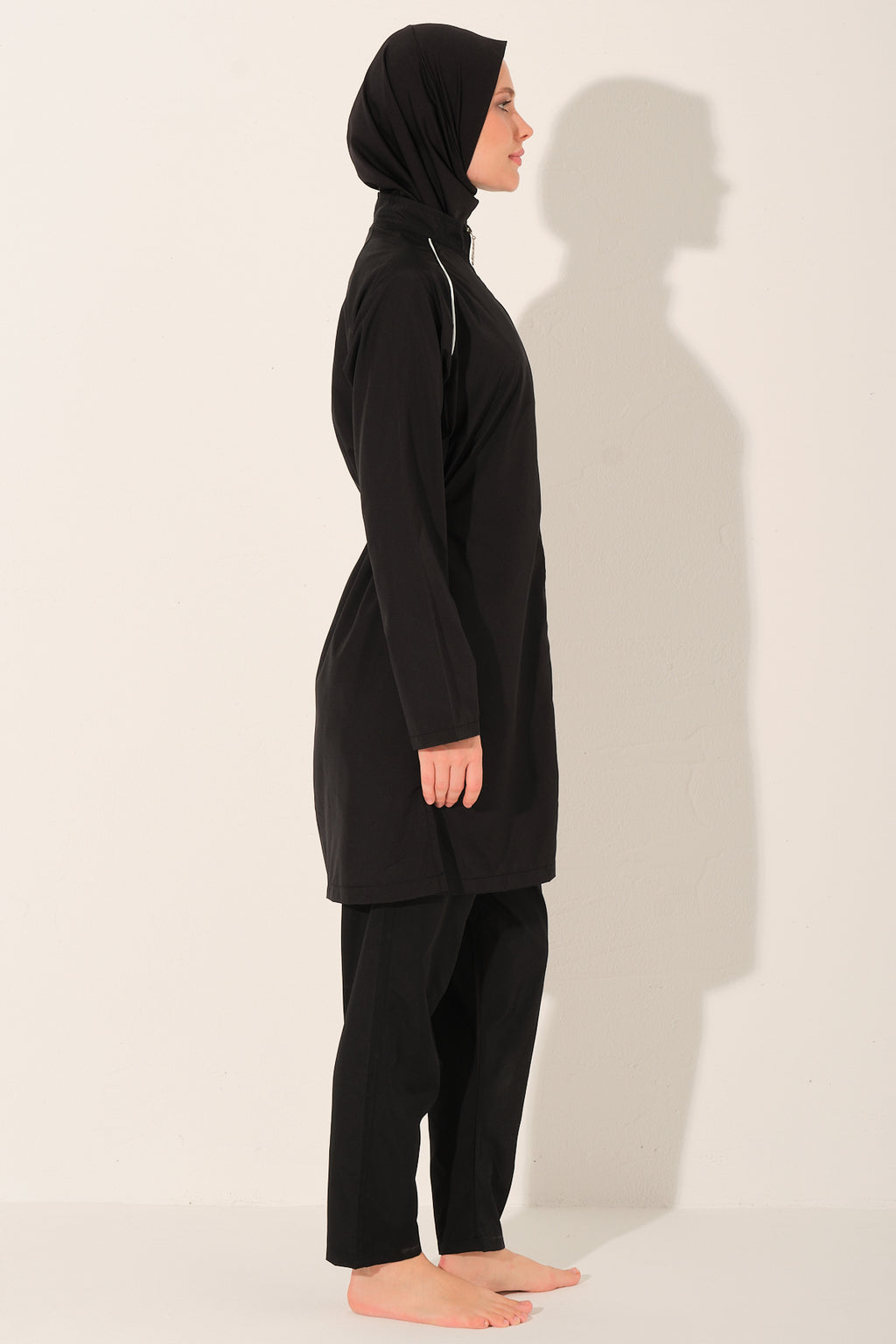 lady wearing a black full-body cover burkini  with white piping details against a white background