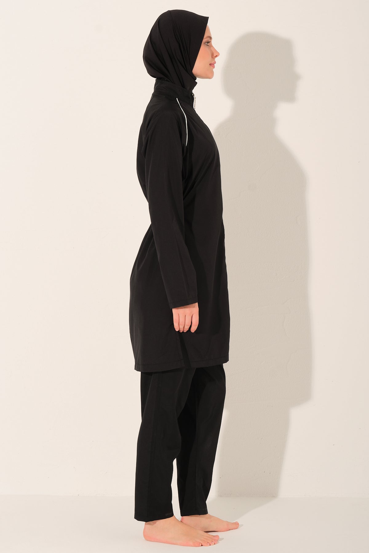lady wearing a black full-body cover burkini  with white piping details against a white background