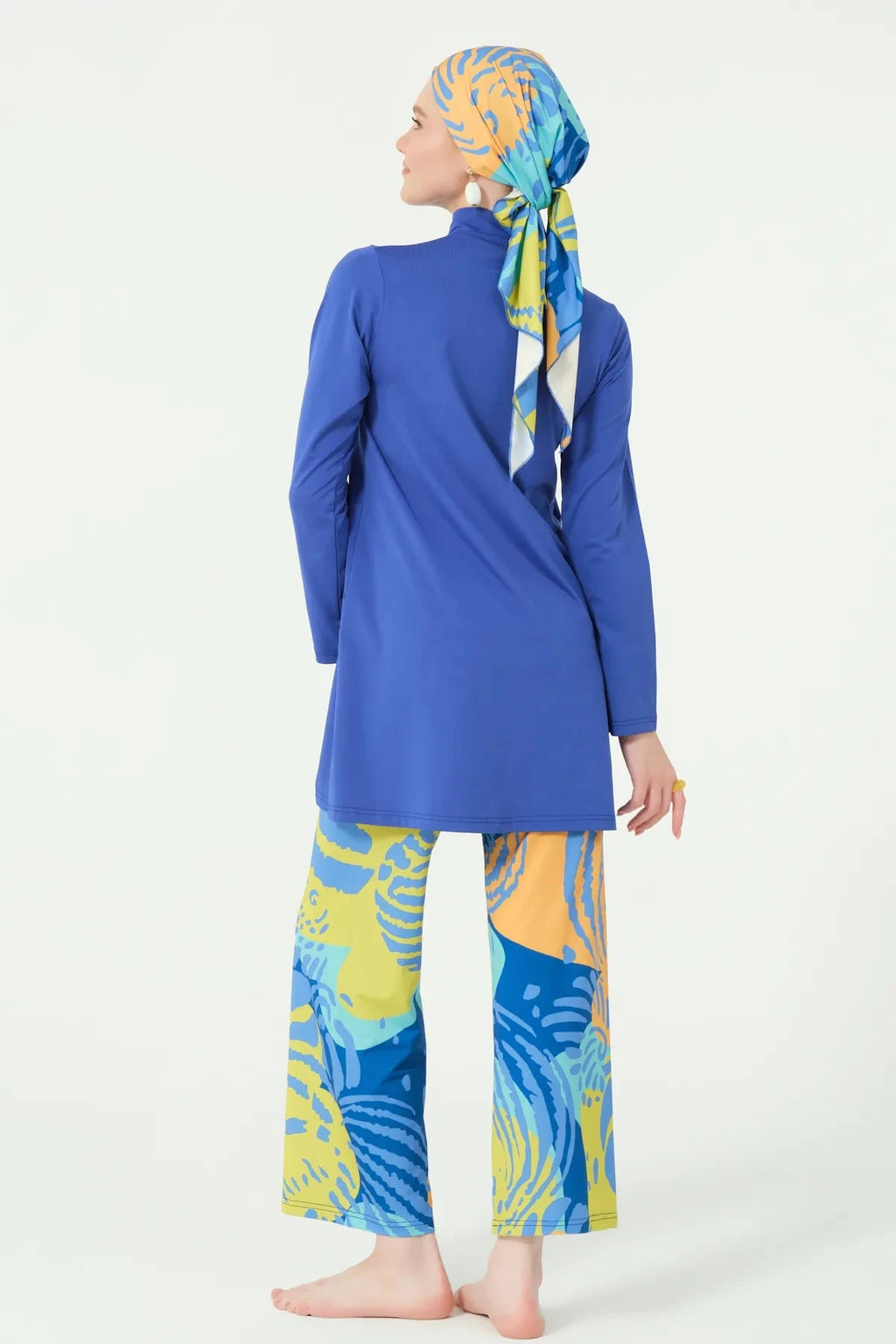 Back view of model wearing blue burkini top and abstract print swim pants.