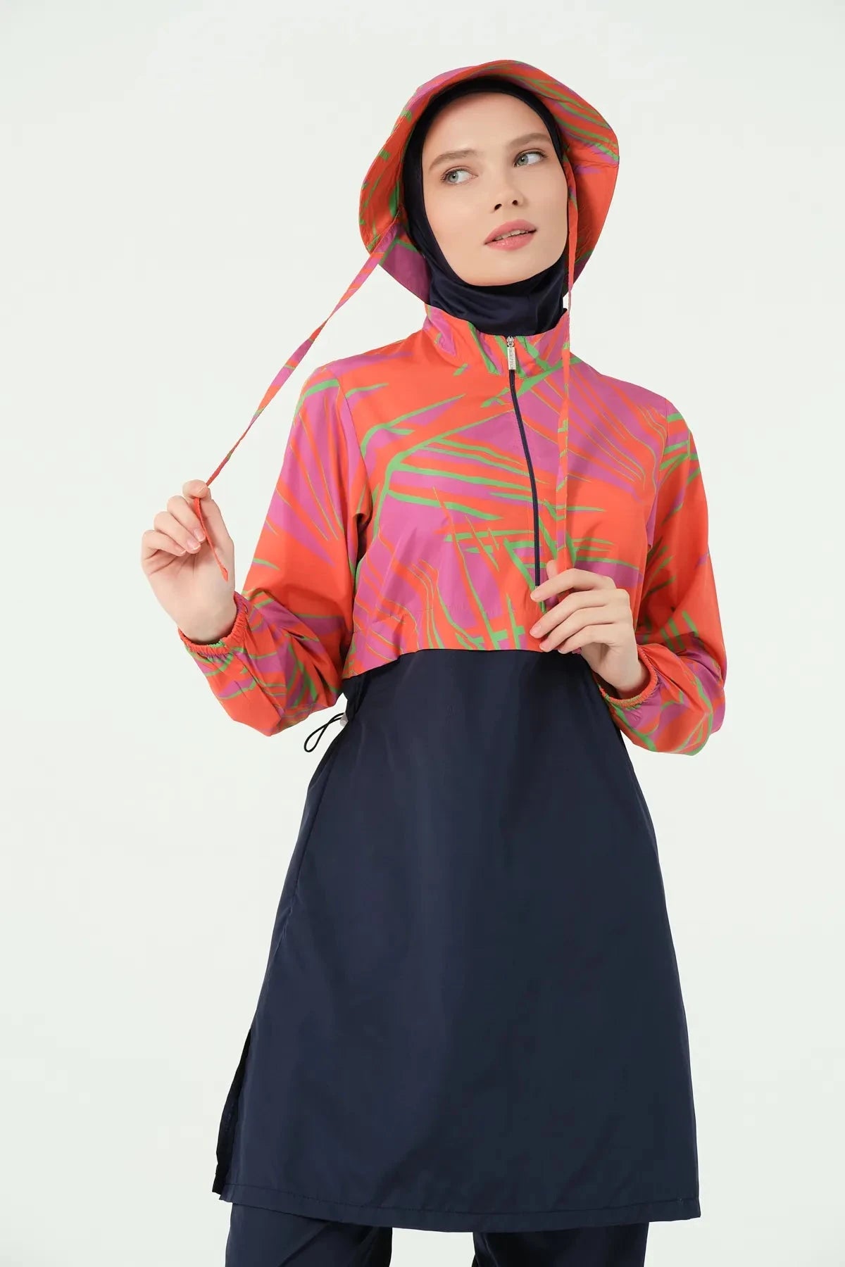 Woman in navy and orange burkini set with bucket hat, adjusting drawstring.