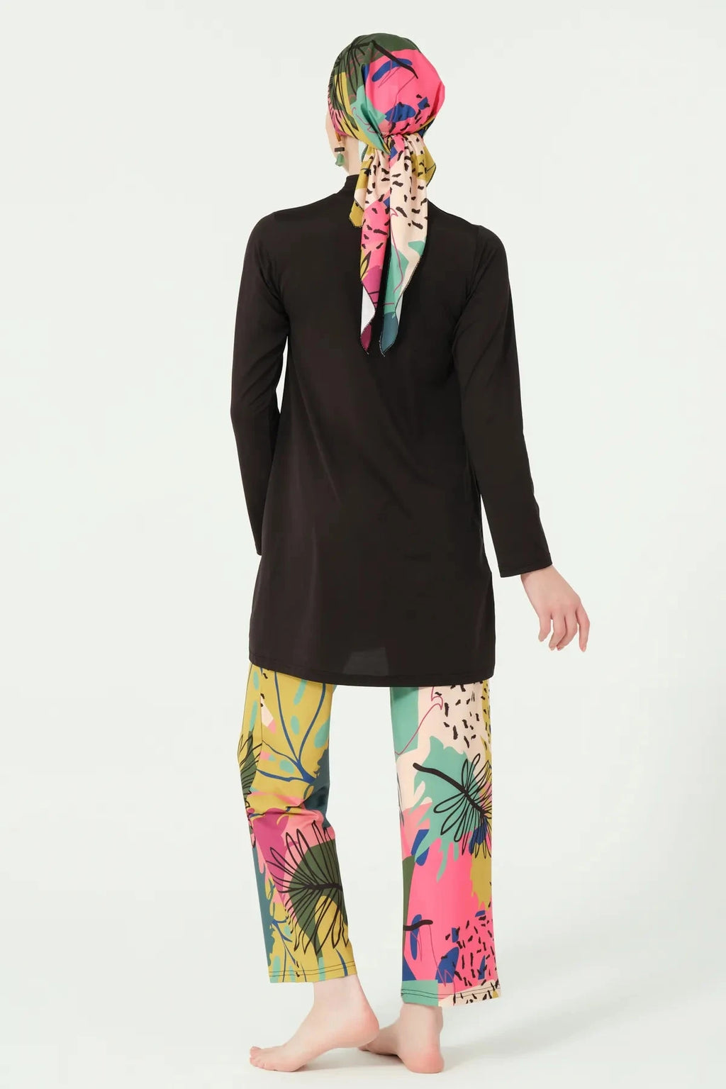 Back view of woman wearing black burkini with vibrant abstract print swim pants.
