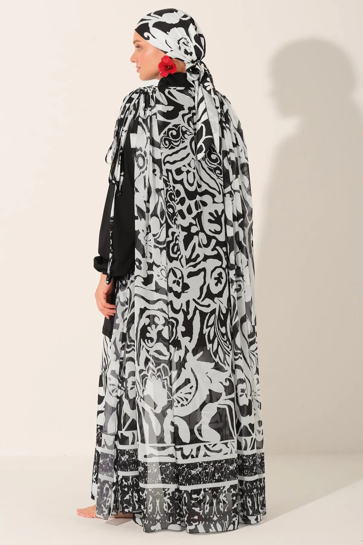 Woman wearing a black and white patterned abaya with a matching headscarf on a plain background