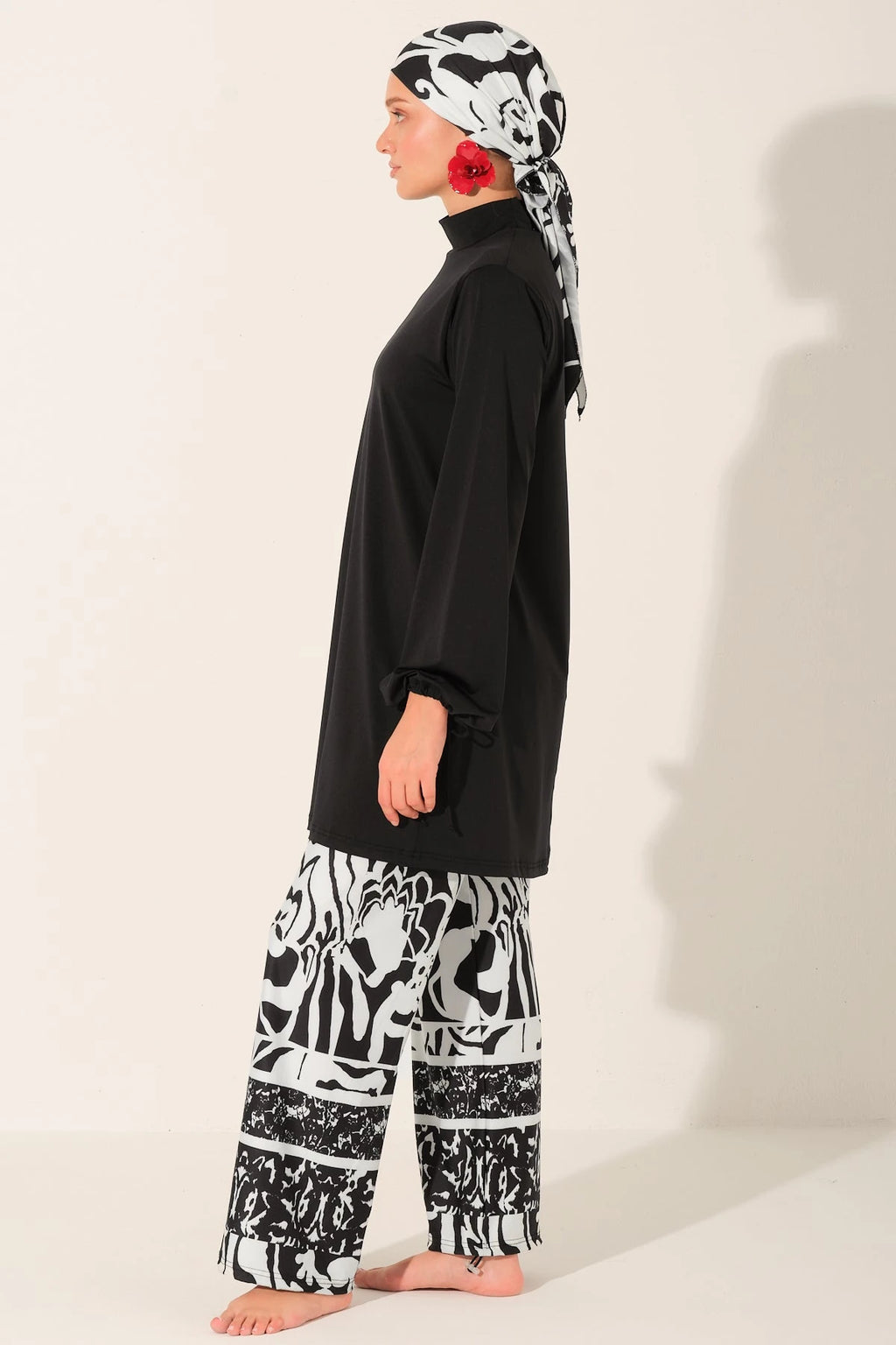 Side view of woman in black top, patterned swim pants, and head scarf.