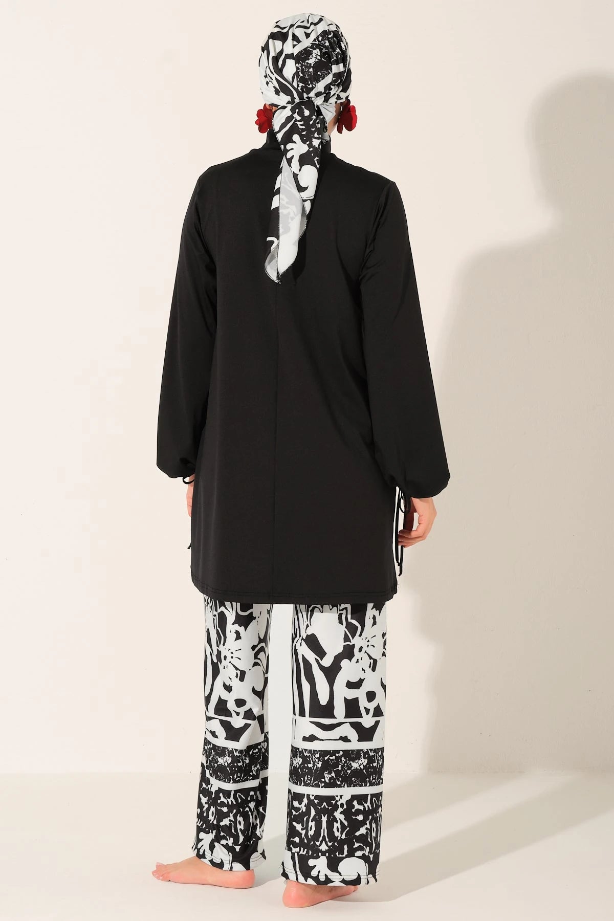 Back view of woman in black top, patterned swim pants, and head scarf.