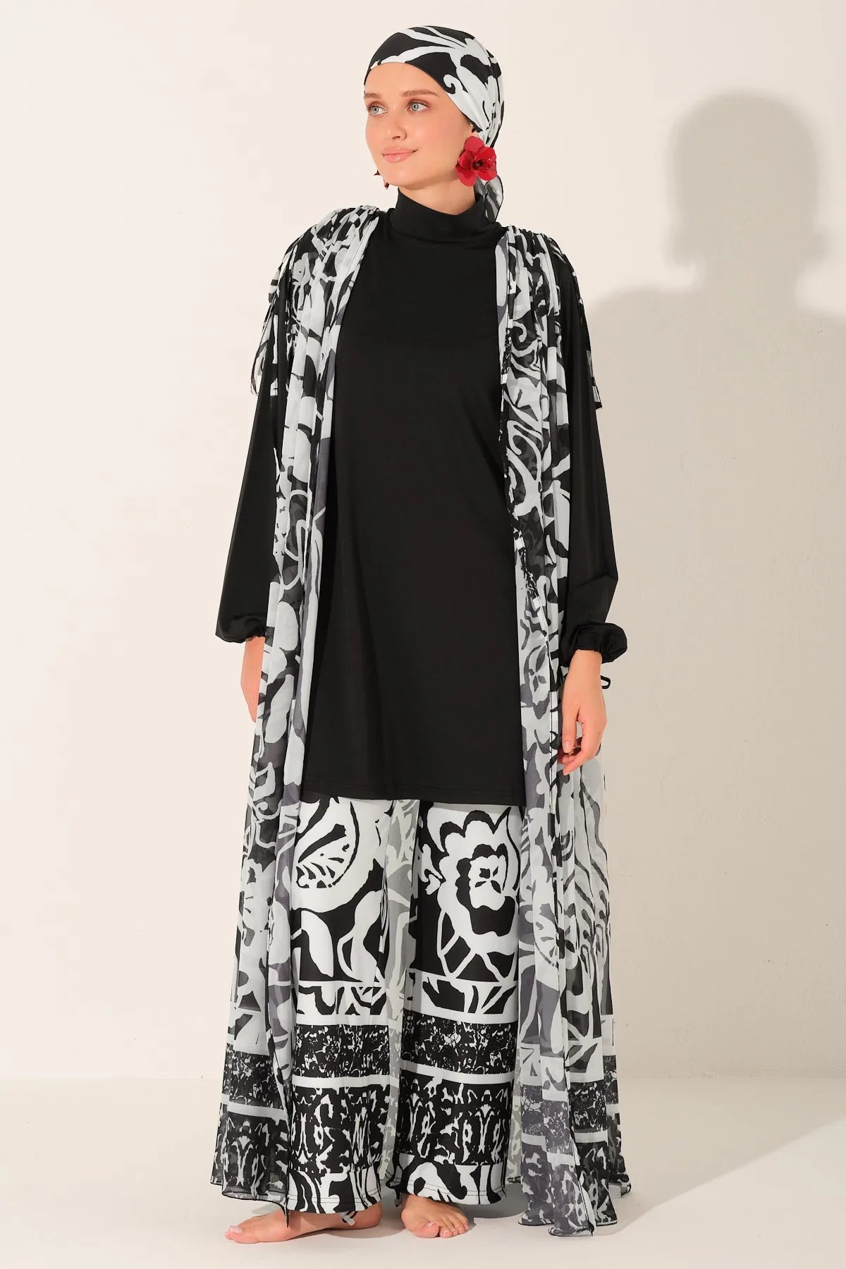 Woman wearing a black and white patterned abaya with a matching headscarf on a white background