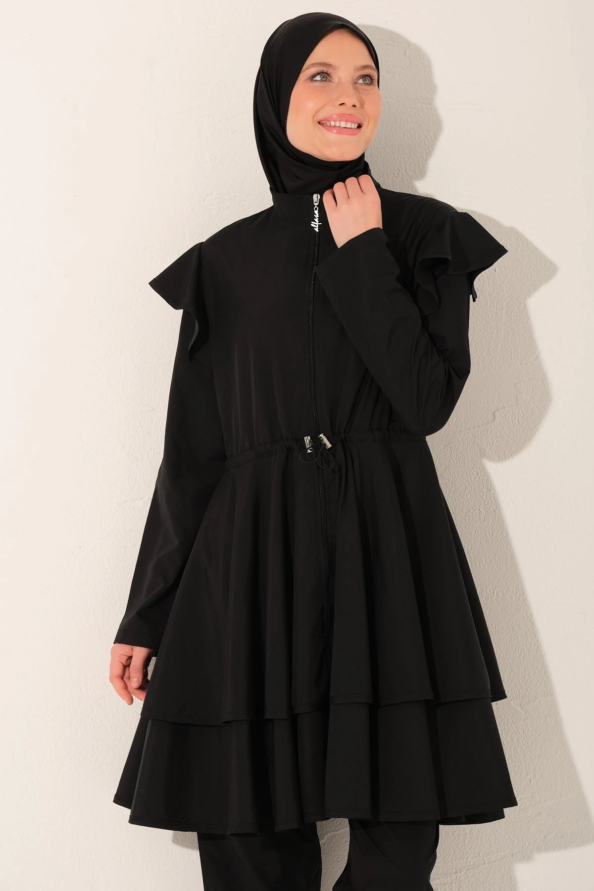 Black ruffle burkini set upper body detail with model adjusting hijab.