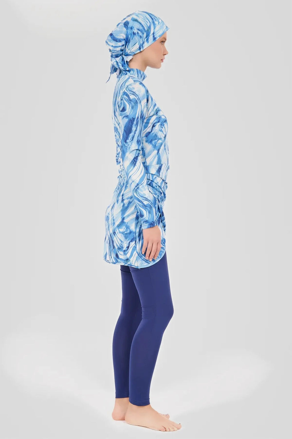 Model in blue wave print burkini top and swim pants, side view.