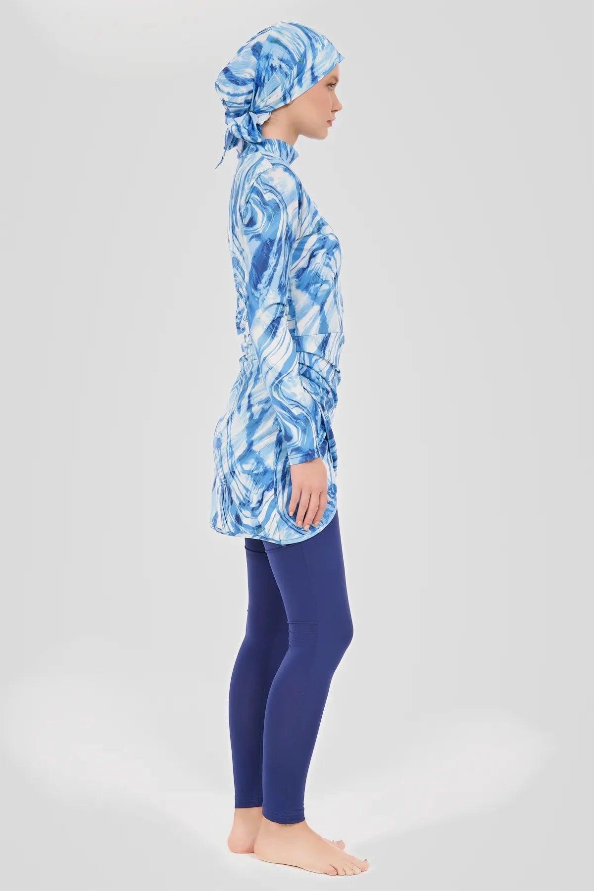 Model in blue wave print burkini top and swim pants, side view.