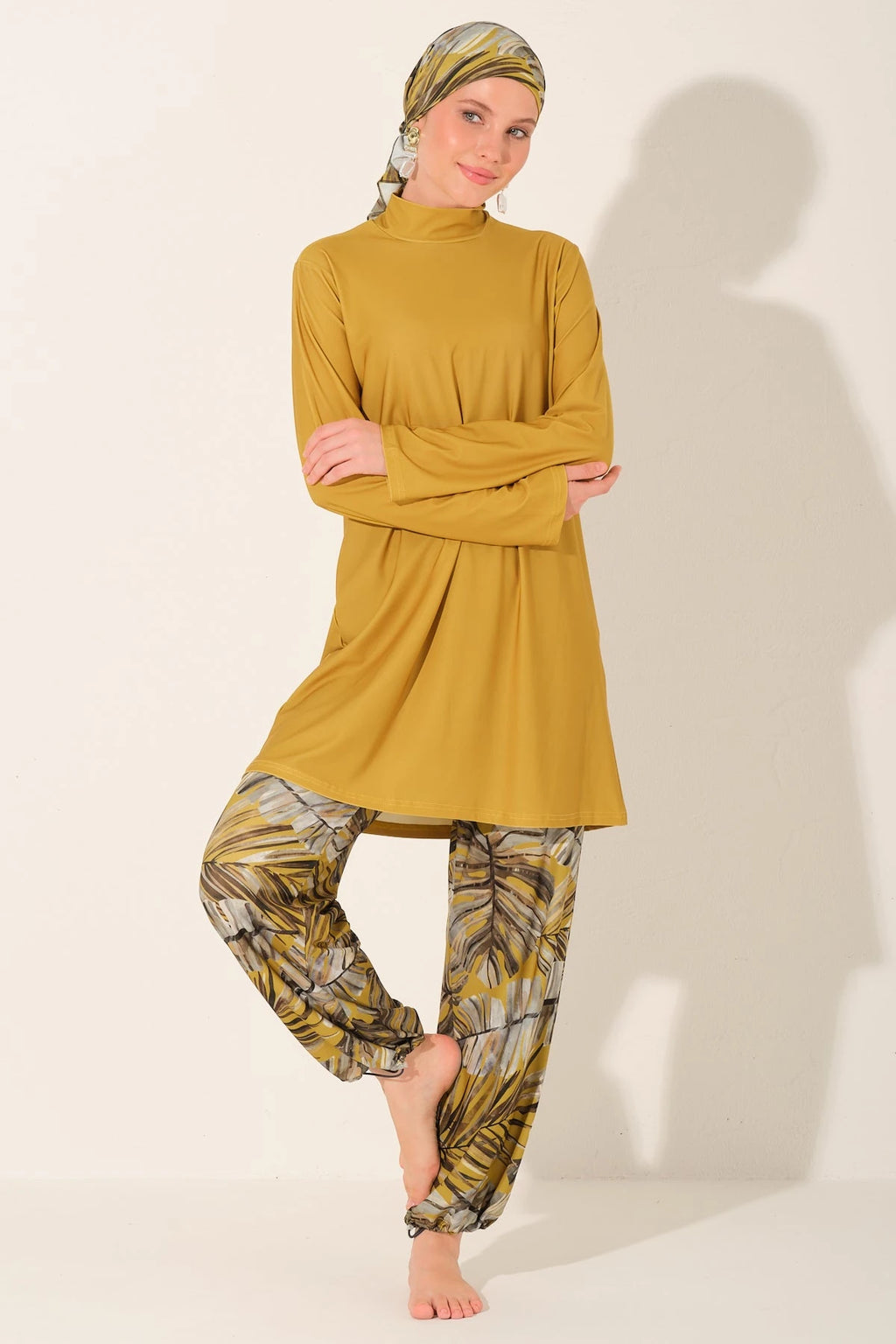 Woman in mustard burkini top and palm print swim pants.