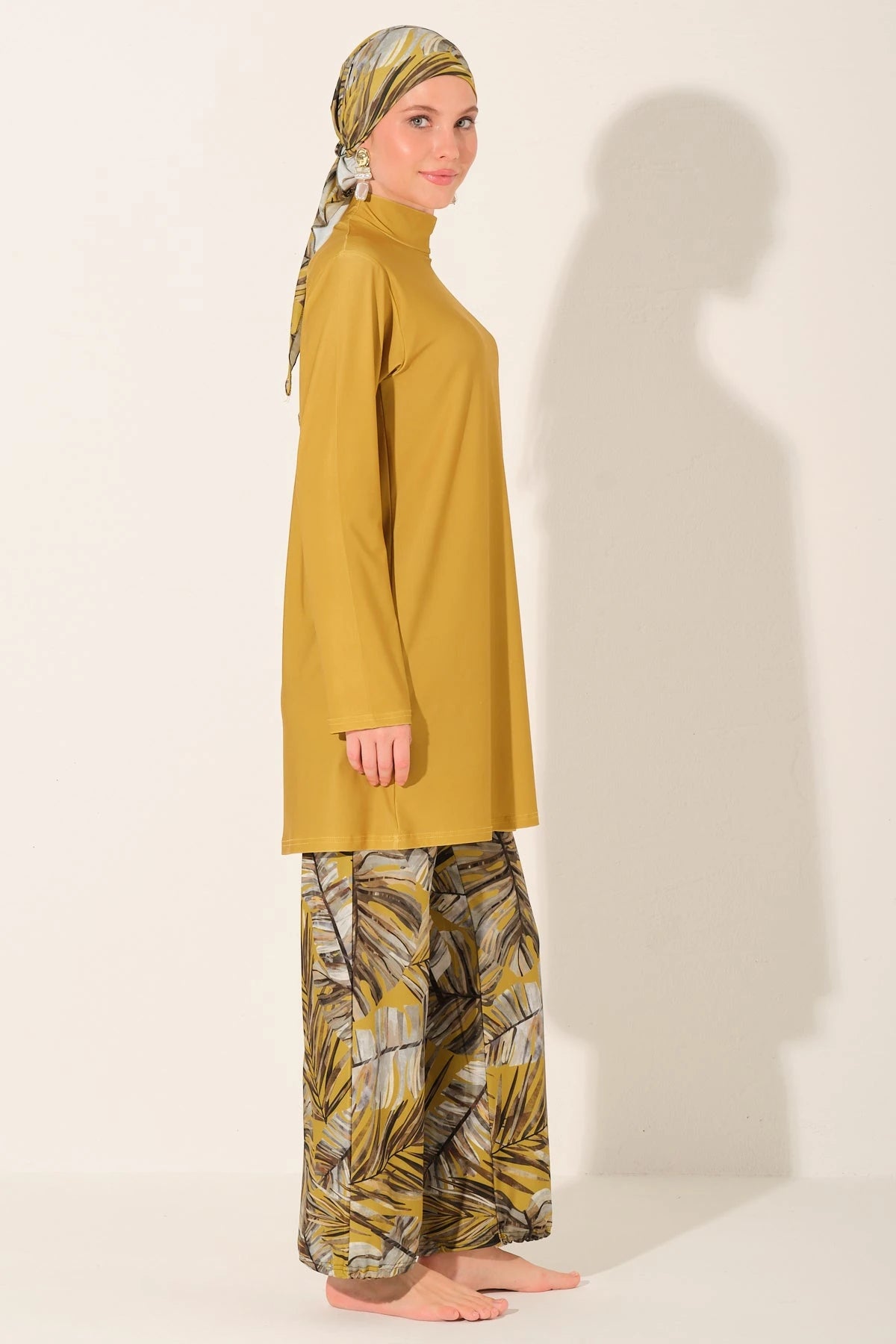 Side view of woman in mustard burkini top and patterned swim pants.