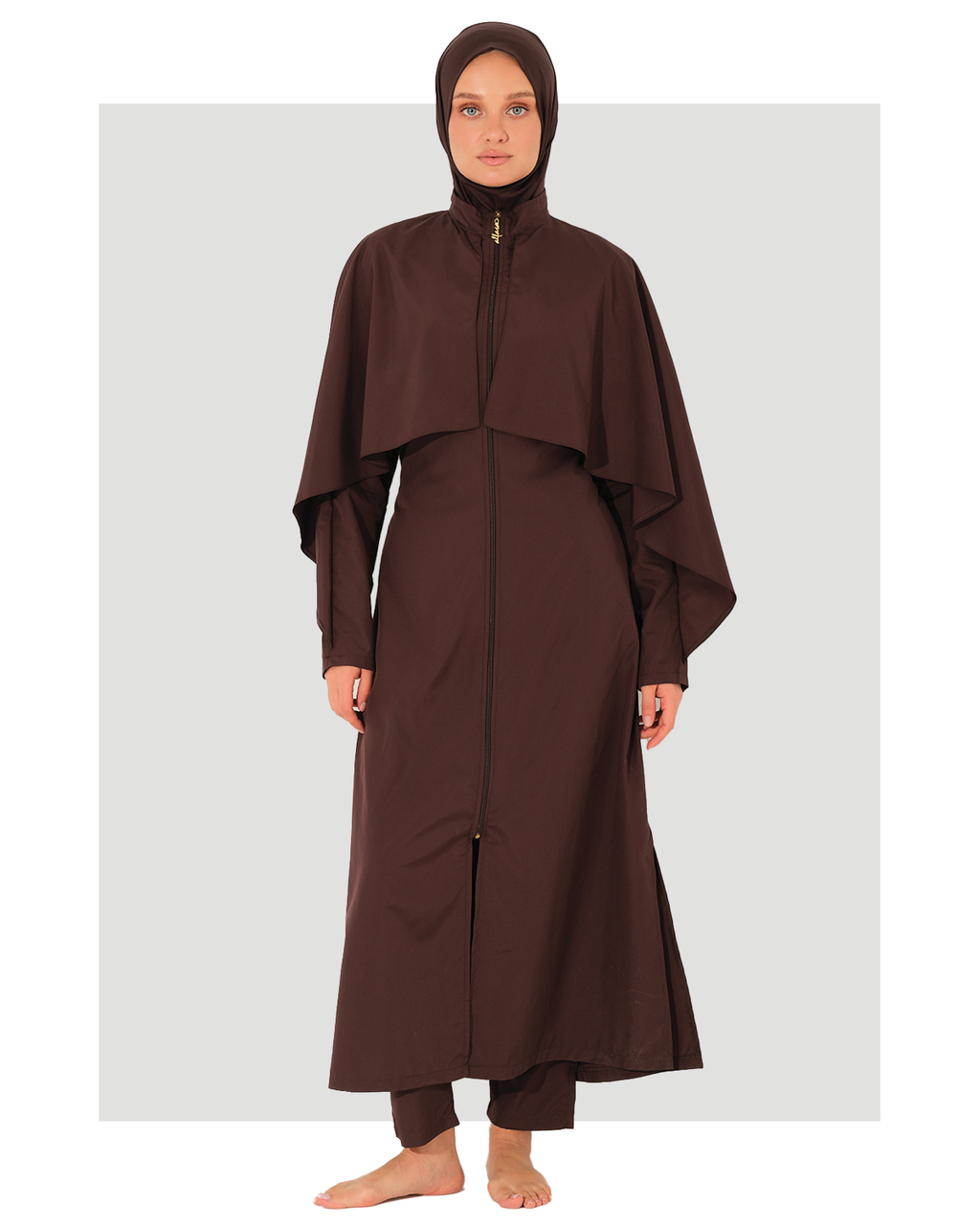 A woman wearing a dark brown modest long-sleeve abaya burkini with a high collar, a front zipper, and a draped cape-style overlay, paired with a matching hijab, standing against a light gray background.