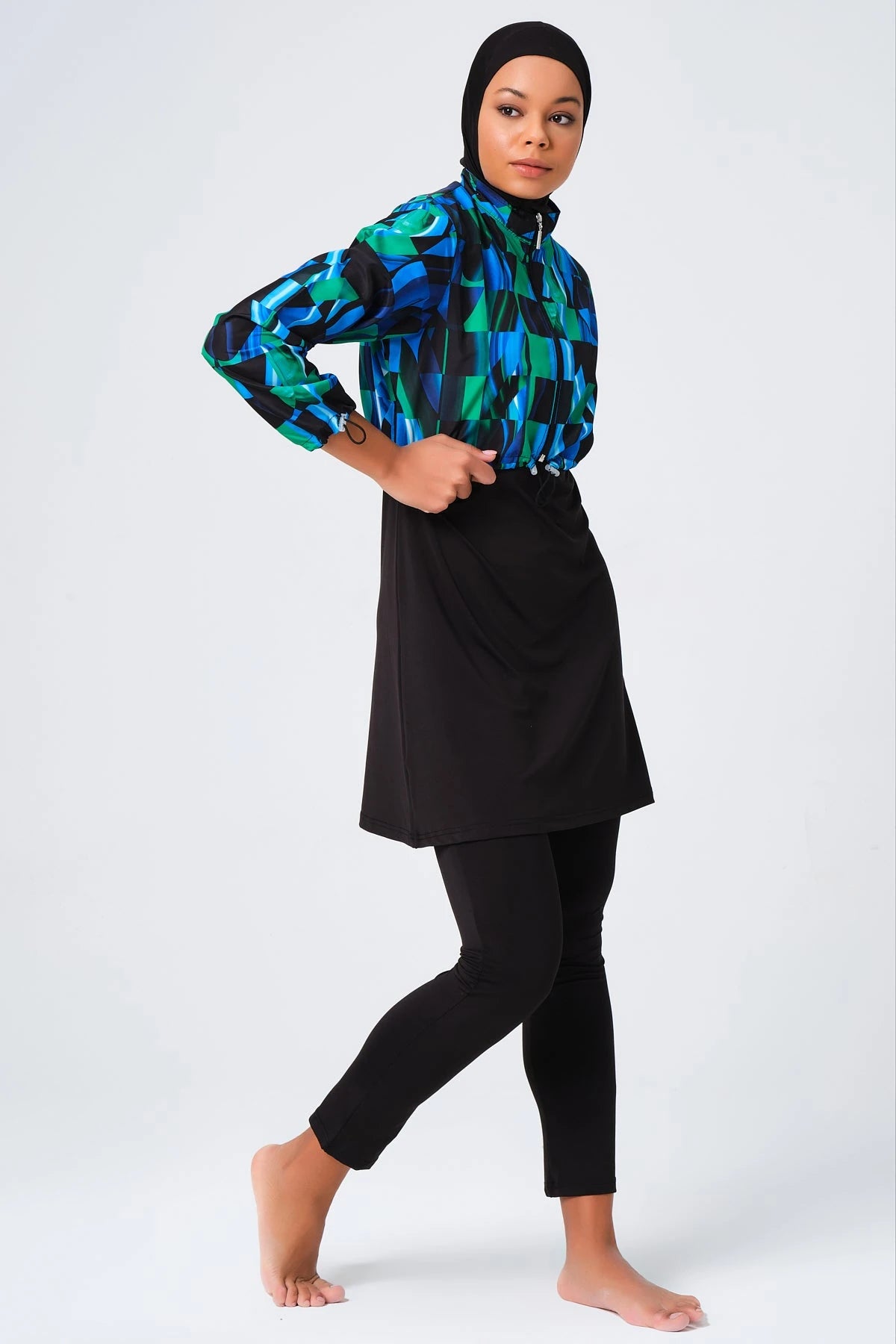 Woman in sporty burkini with blue green abstract print jacket walking.