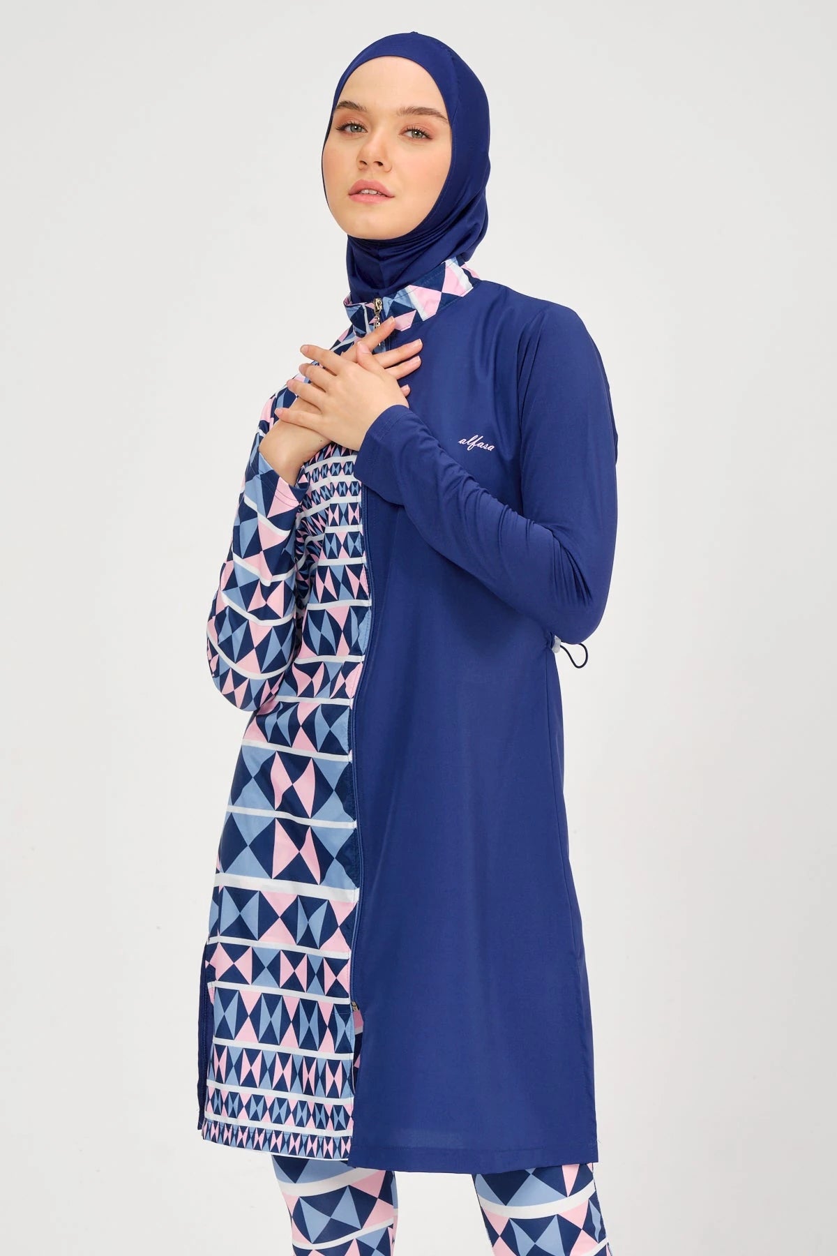 Model in blue and geometric burkini with hands near chest.