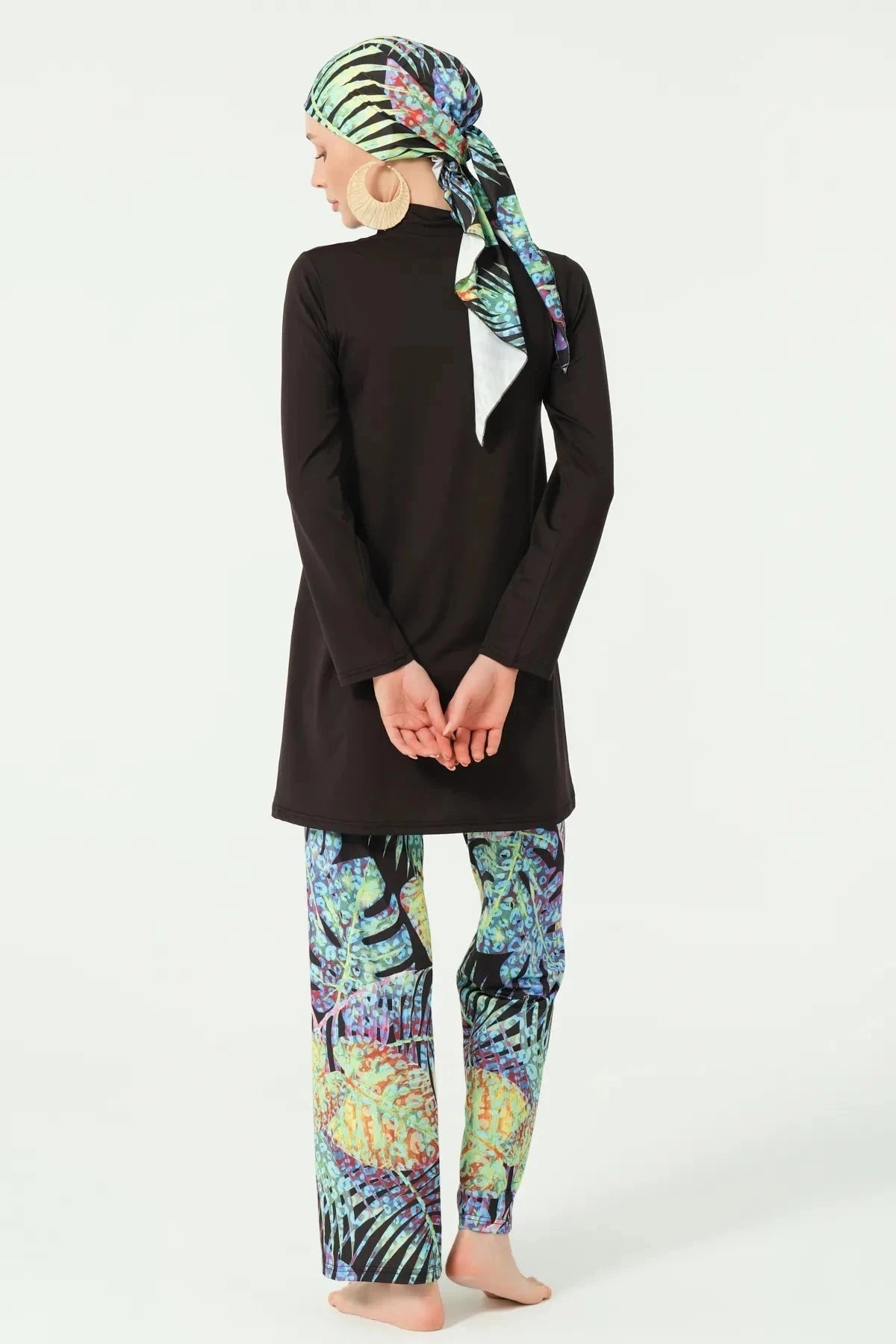 Back view of black burkini with vibrant tropical print pants and head covering.