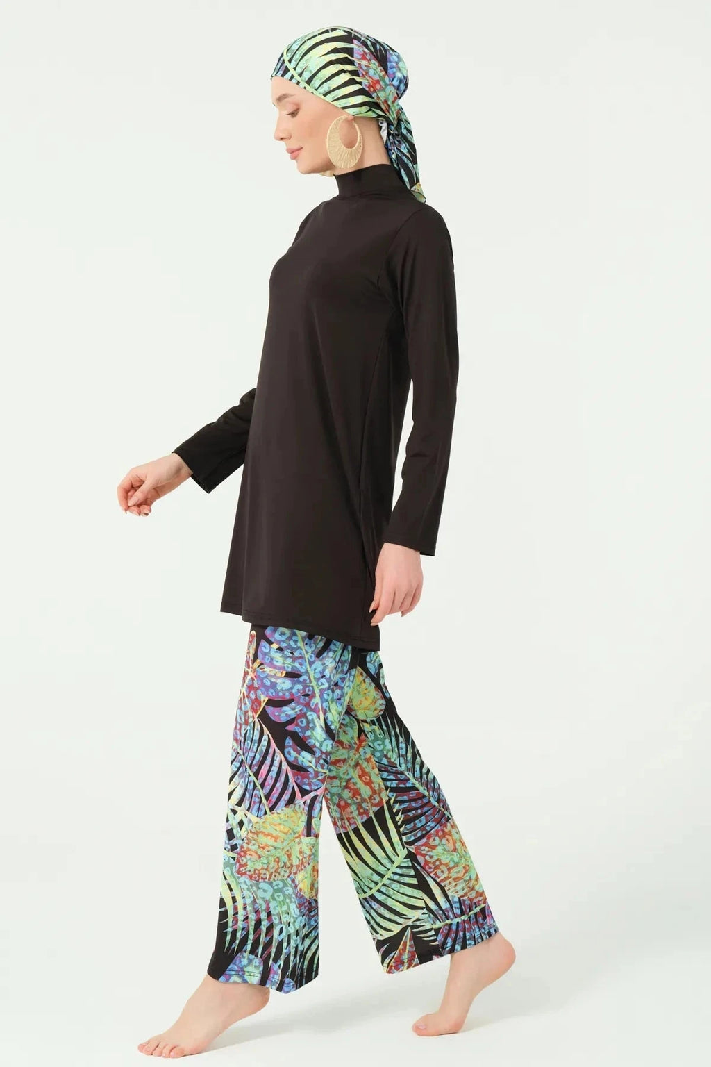 Side view of black burkini with tropical print pants in walking pose.