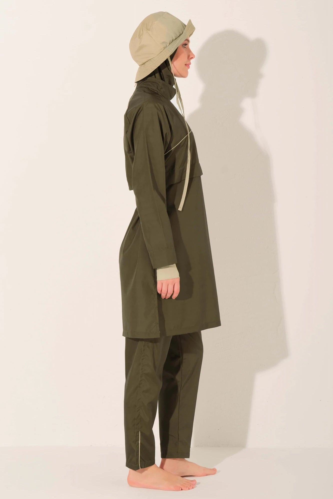 Woman in olive trail burkini and beige hat, side profile.