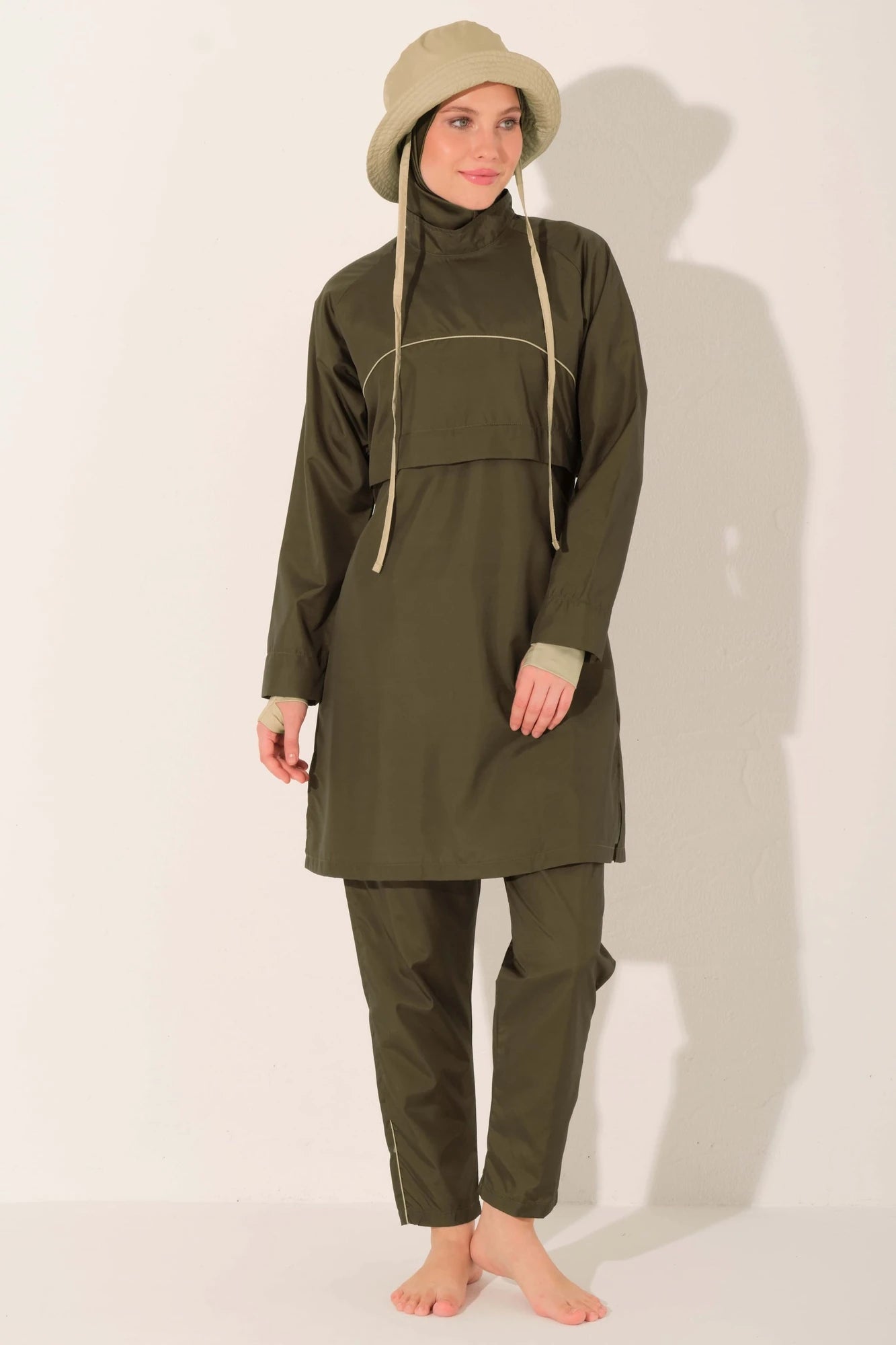 Full body view of woman in olive trail burkini and beige hat.