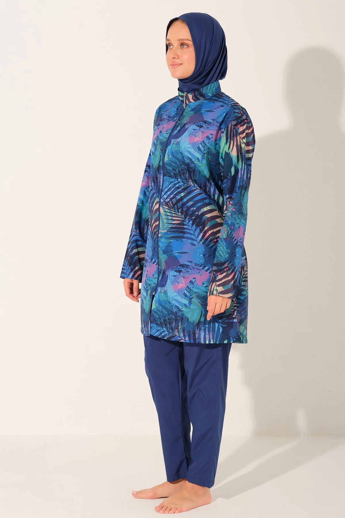 Model wearing blue tropical print burkini set, side view, on light background.
