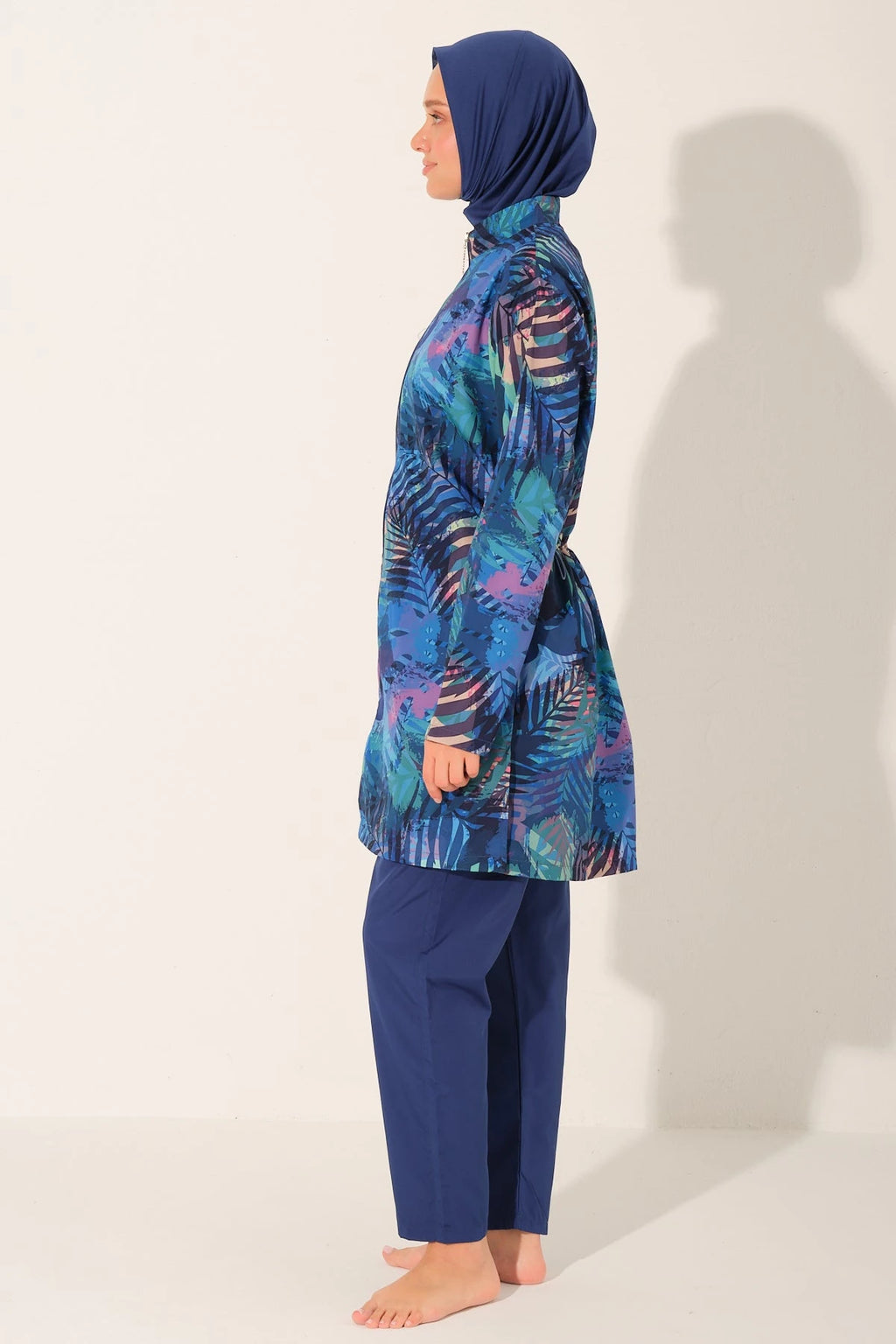 Model in blue tropical print burkini set, profile view, standing calmly.