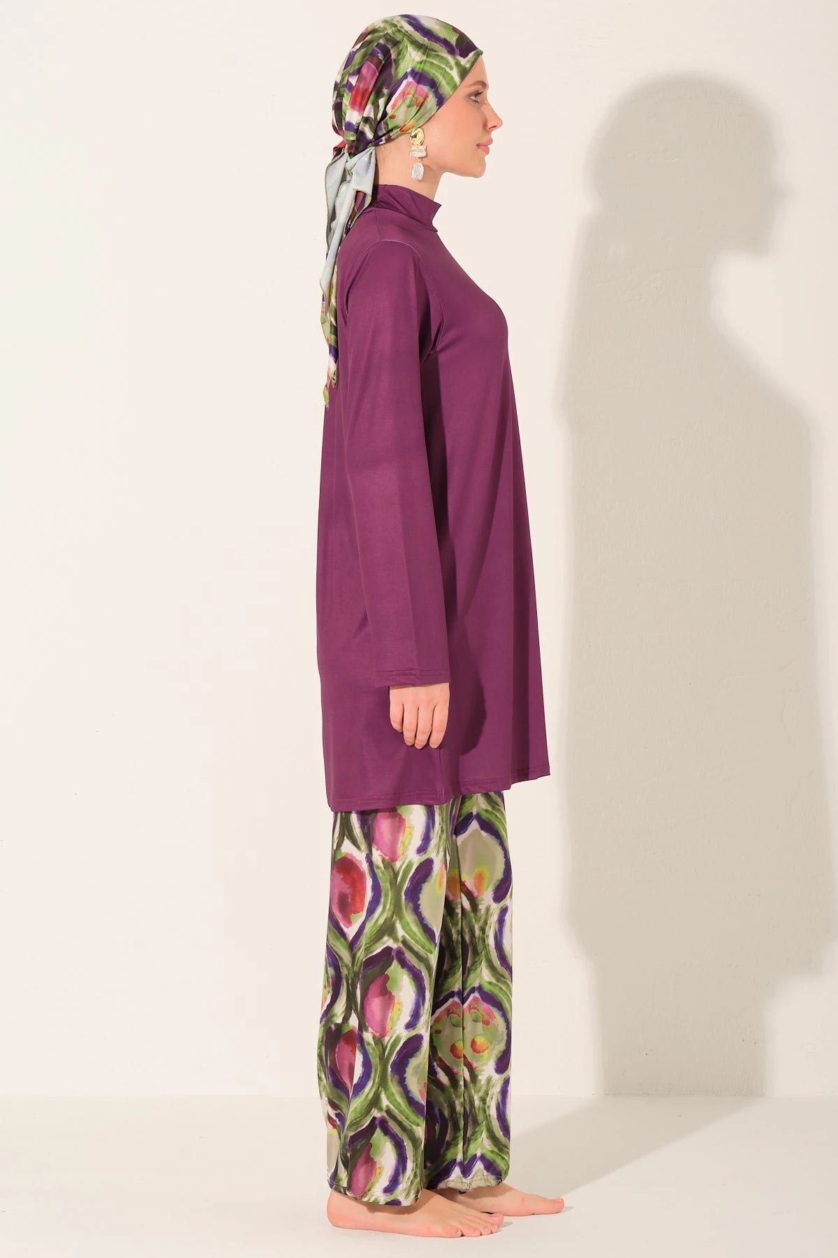 Side view of plum burkini set with abstract peacock print pants and headscarf.