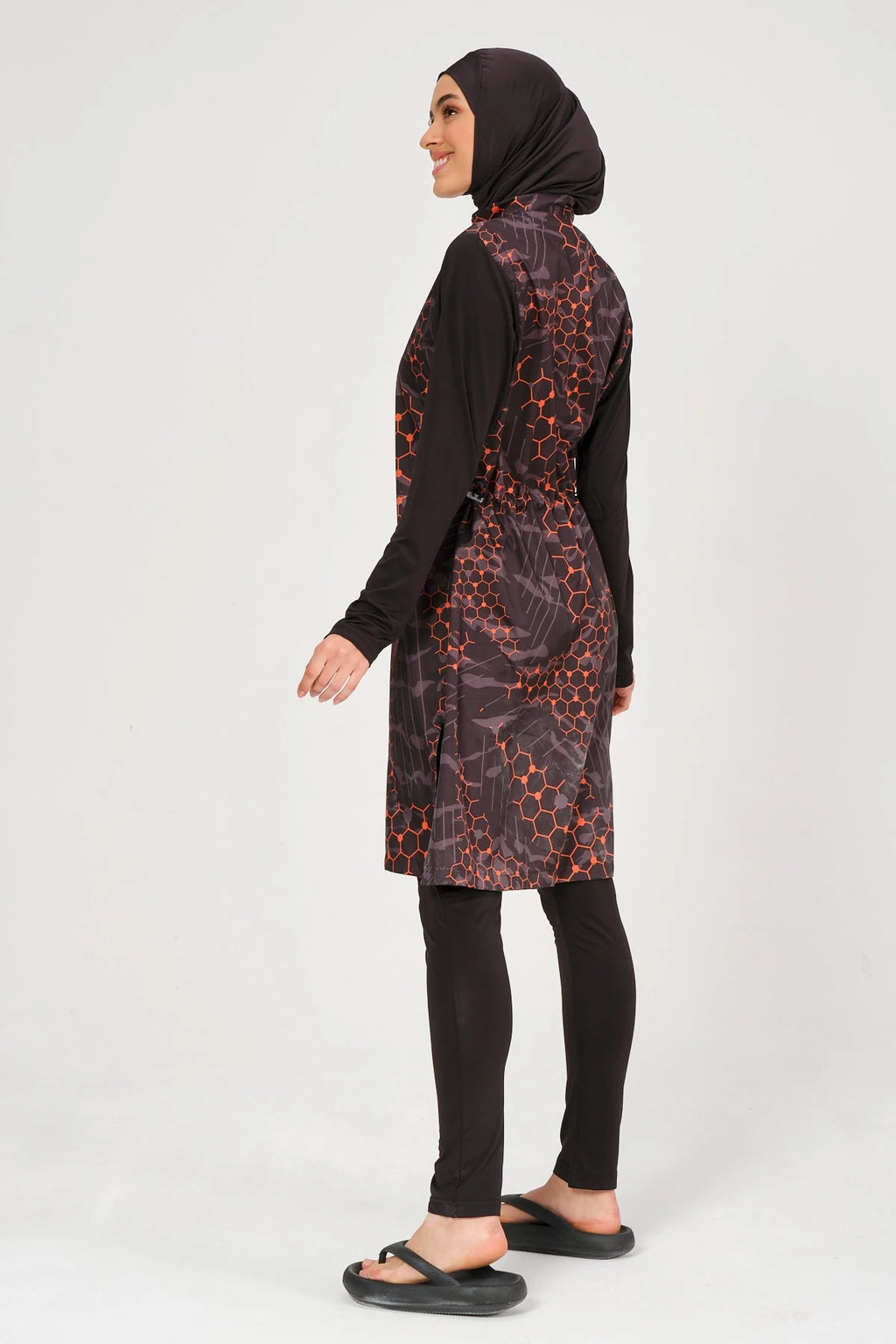 Model in orange and black patterned burkini set, side view, looking right.