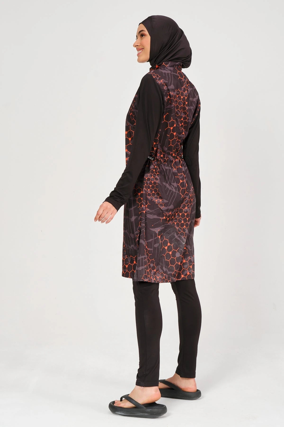 Model in orange and black patterned burkini set, side view, looking right.