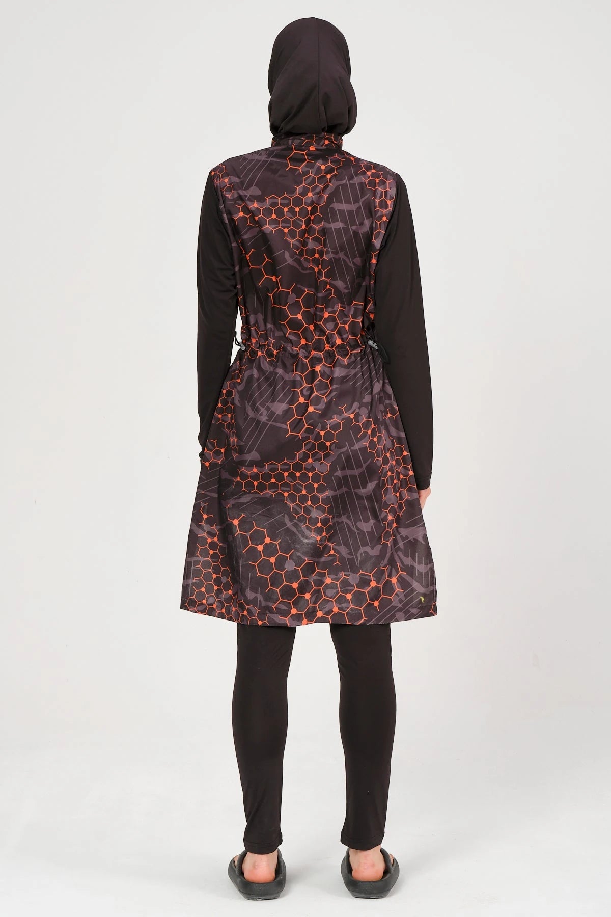 Model in orange and black patterned burkini set, back view, full coverage.