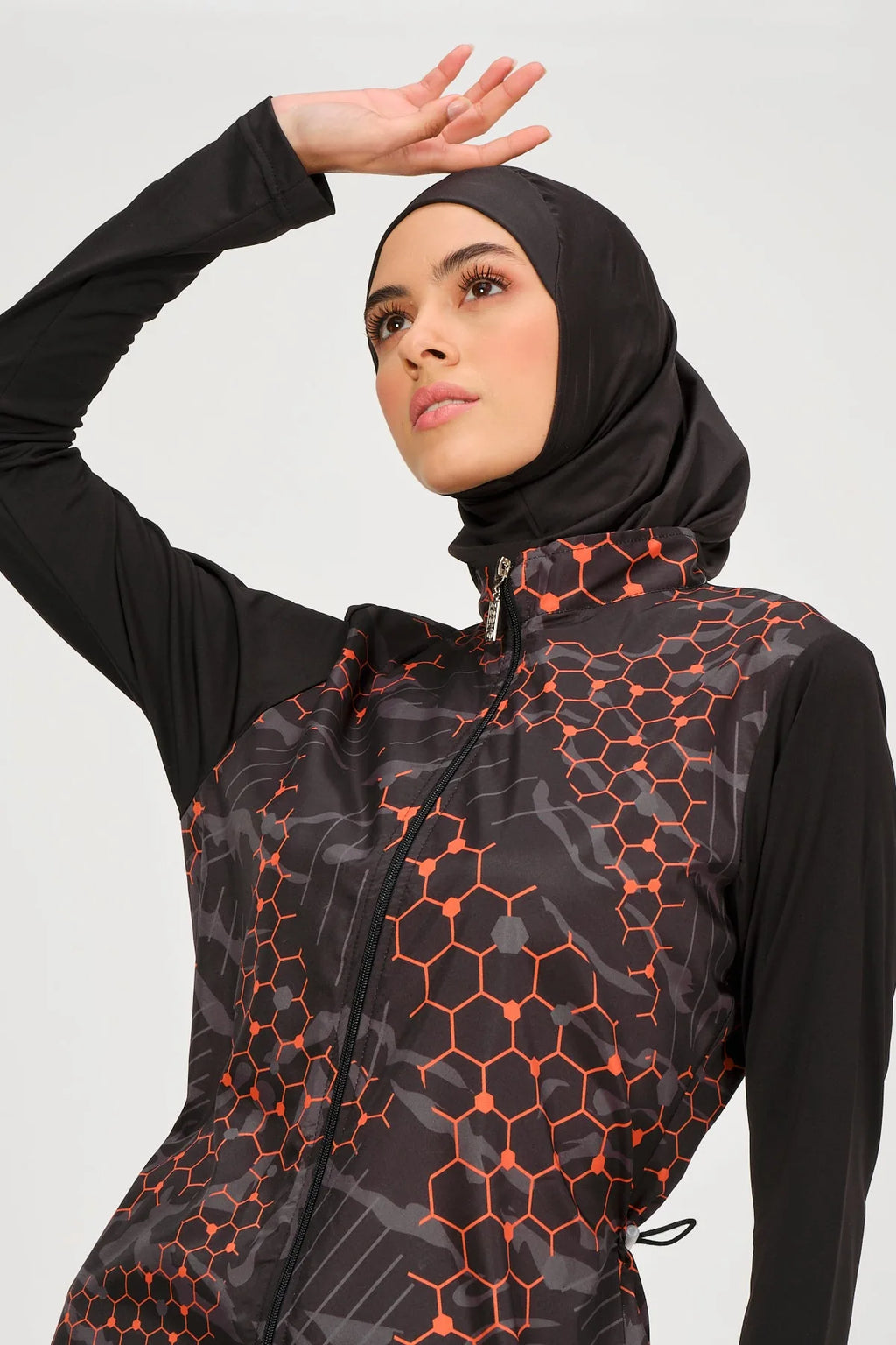 Close-up of model in orange and black burkini top and black swim hijab.