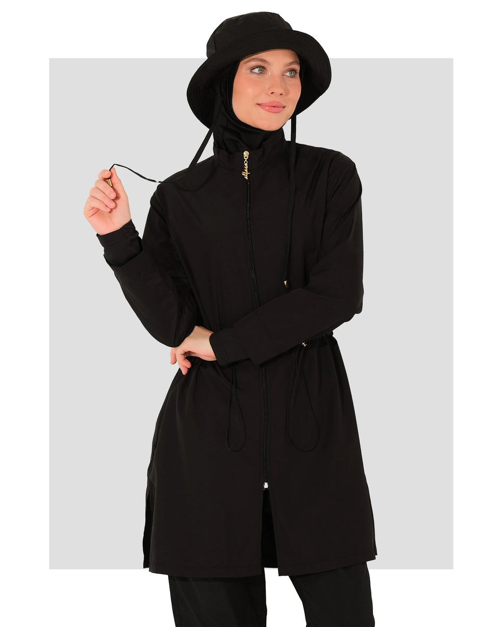 Woman in black burkini set with bucket hat, holding drawstring.