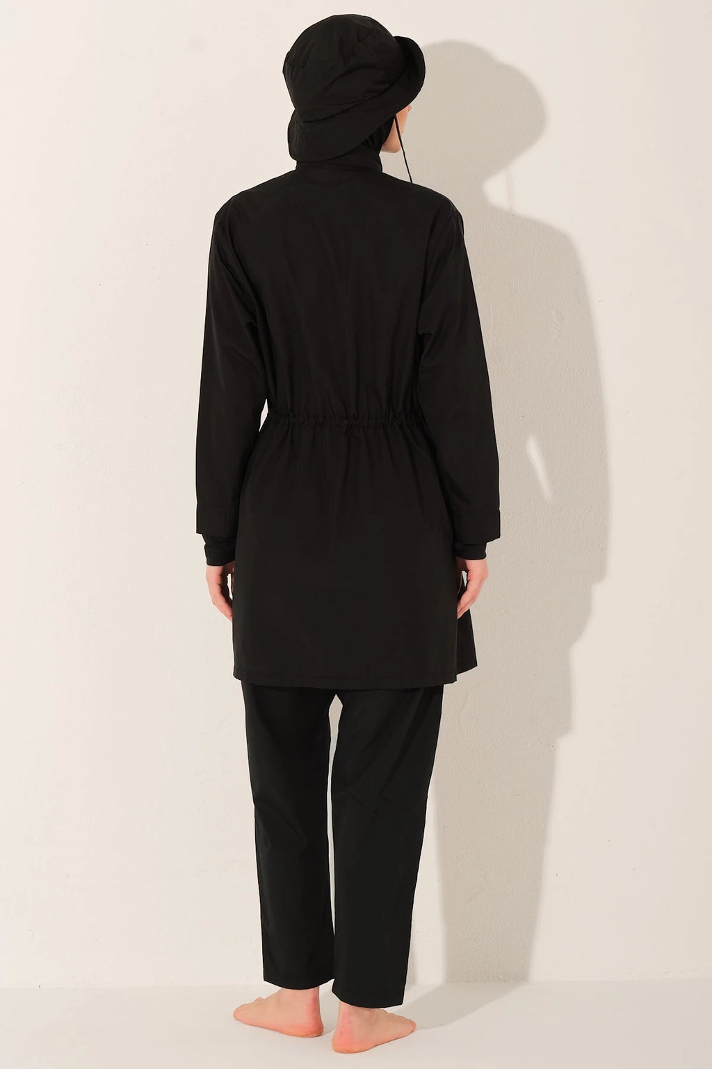 Back view of woman wearing black burkini set with matching bucket hat.