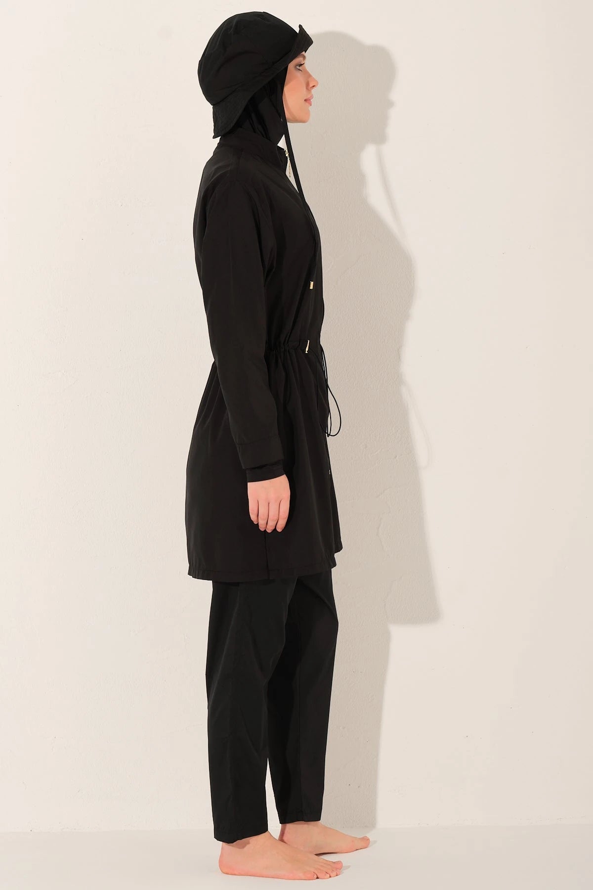 Side profile of woman in black burkini set with bucket hat.