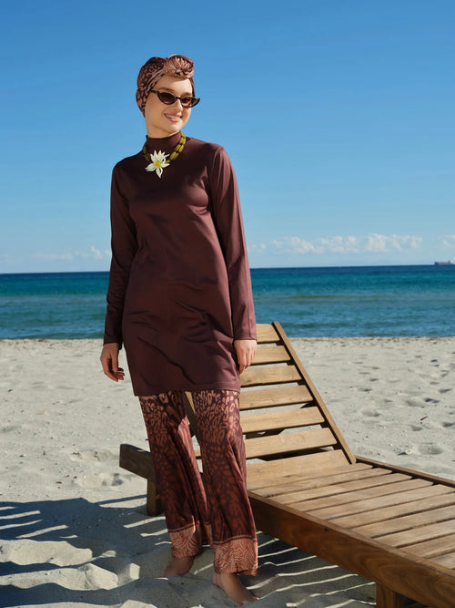 Woman in mocha print burkini and sunglasses on a sunny beach.