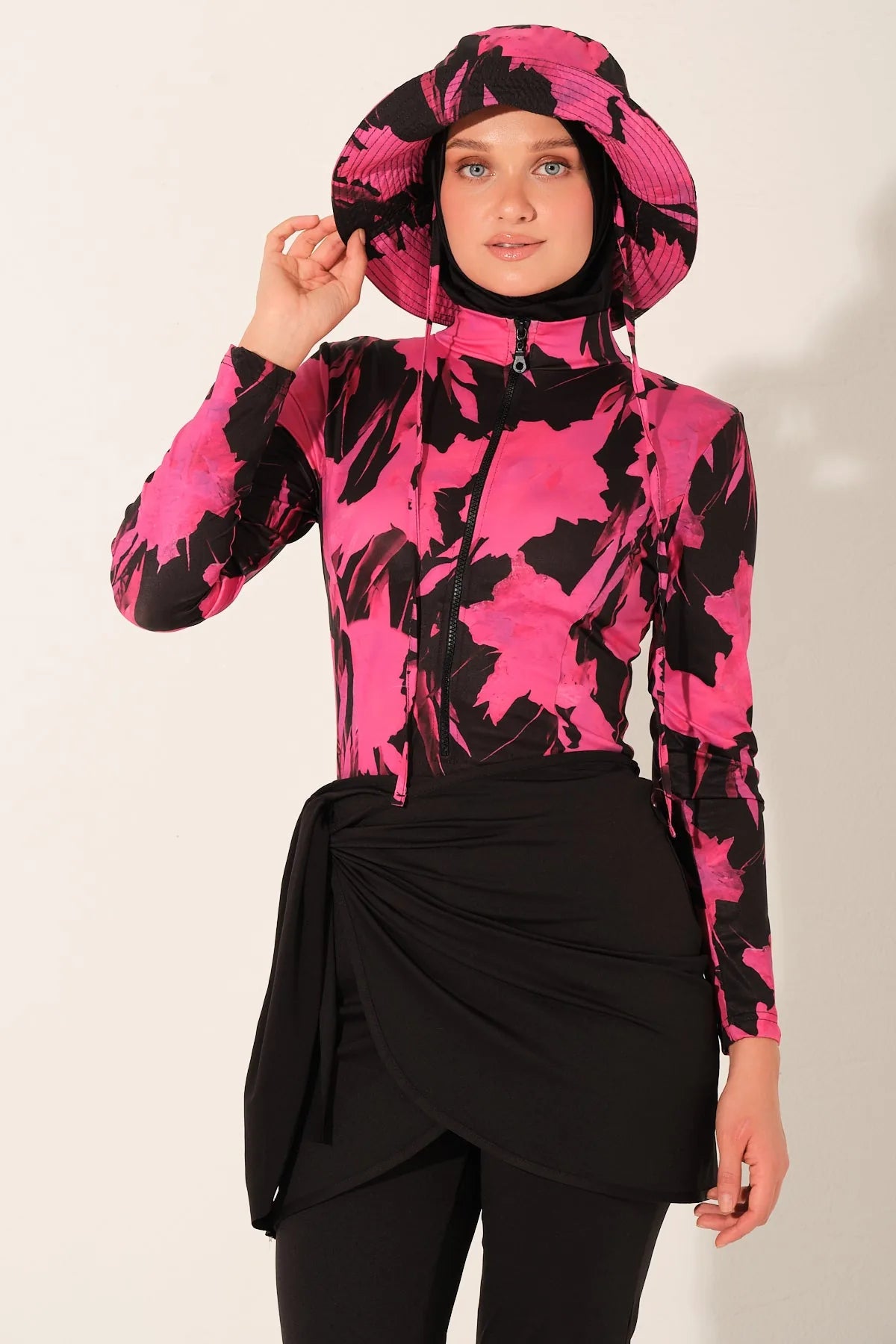 Woman in active floral burkini set, adjusting hat, front.