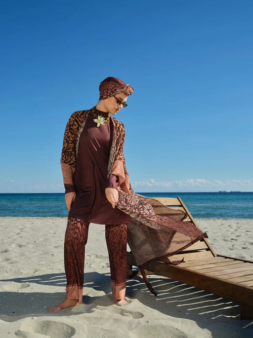 Model in mocha print burkini with open chiffon kimono on beach.
