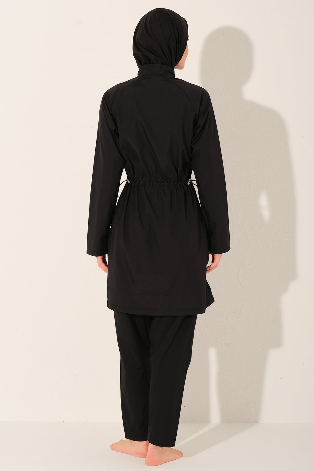 women  wearing a black modest swimsuit with white piping details outfit with a hijab on a white background