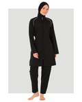 A woman modeling a black modest swimwear set consisting of a long-sleeve high-neck swimsuit with white piping details, matching black swim pants, and a black hijab, set against a light gray background.
