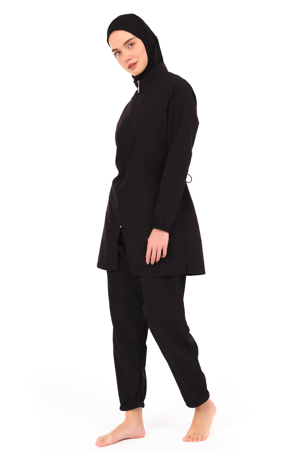 Model wearing black burkini tunic with drawstring waist, looking over shoulder.