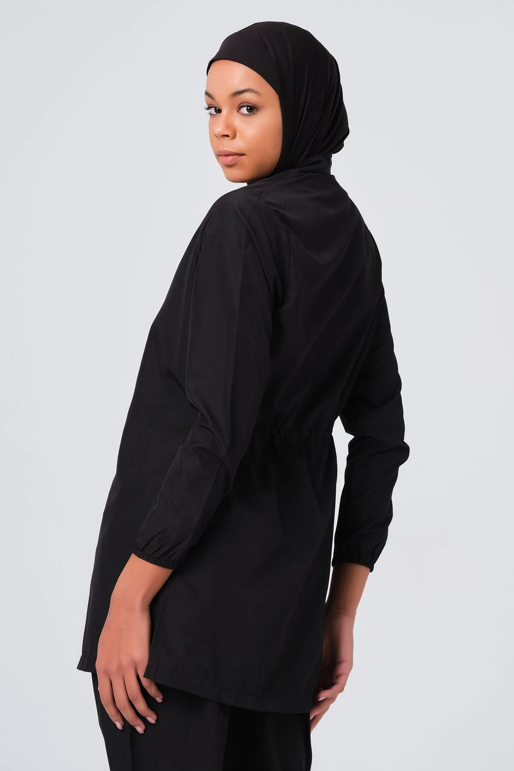 Model wearing black burkini tunic with drawstring waist, looking over shoulder.