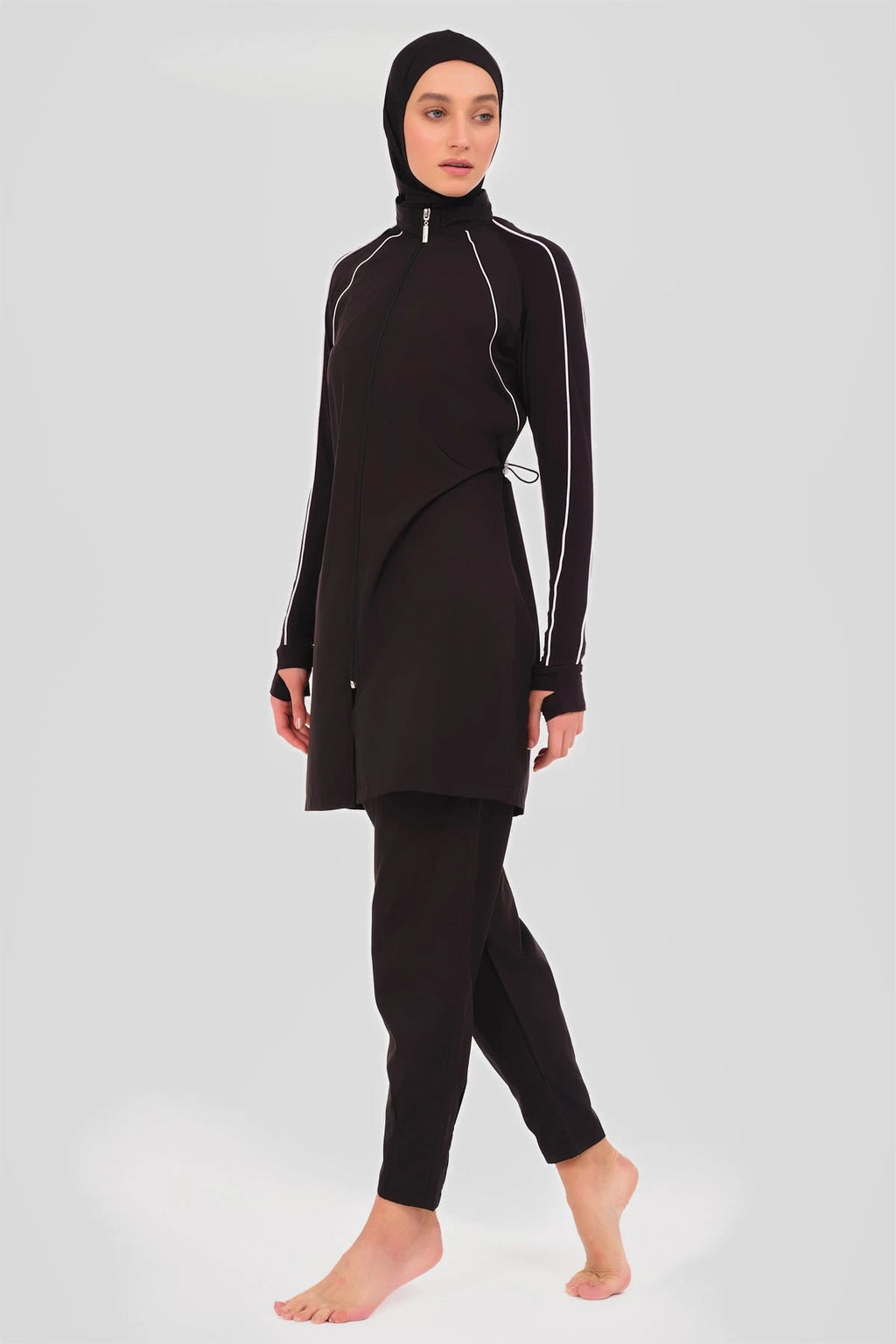 Model in black sporty burkini with white piping, side view.