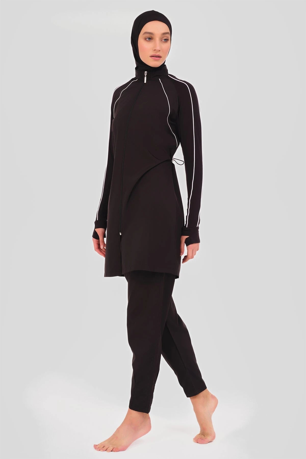 Model in black sporty burkini with white piping, side view.