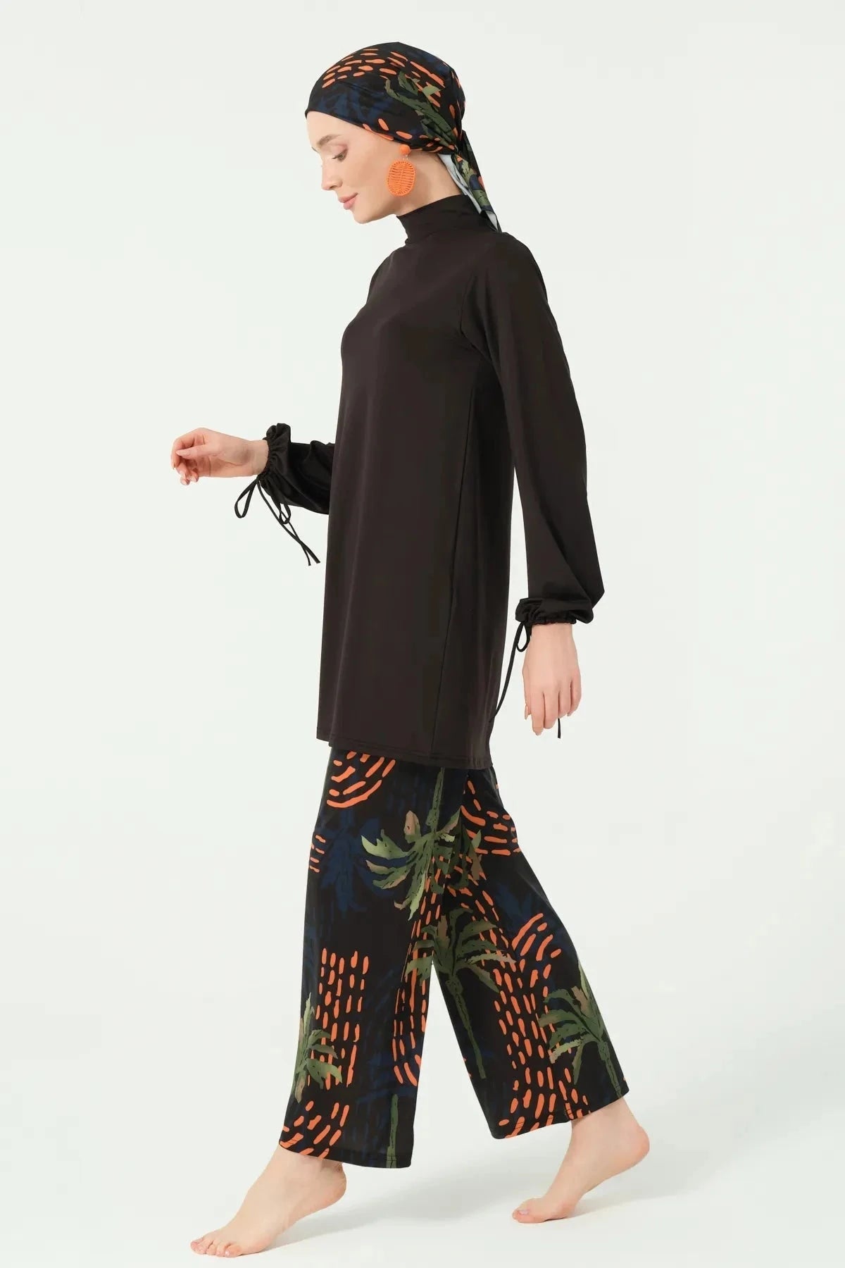 Model in black burkini set with tropical print pants walking sideways.