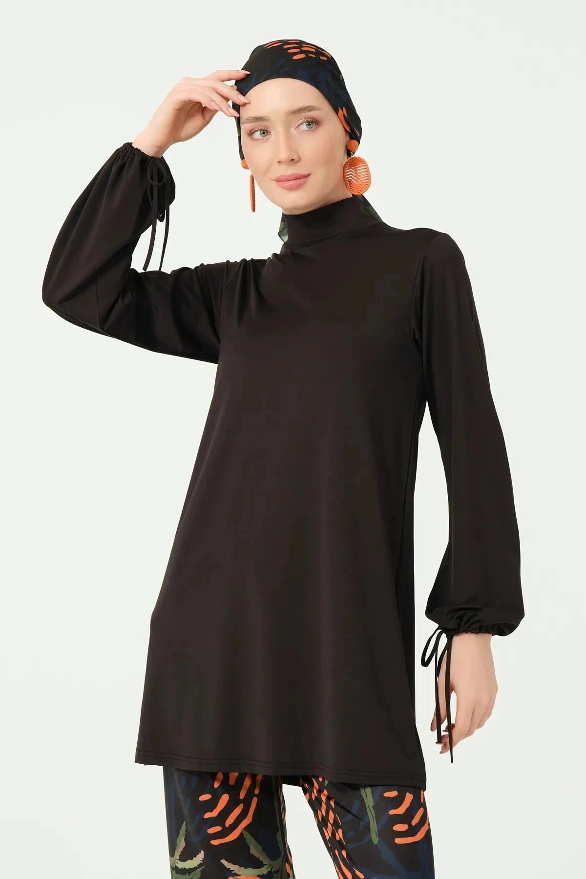 Front view of black burkini set, model adjusting tropical print head covering.