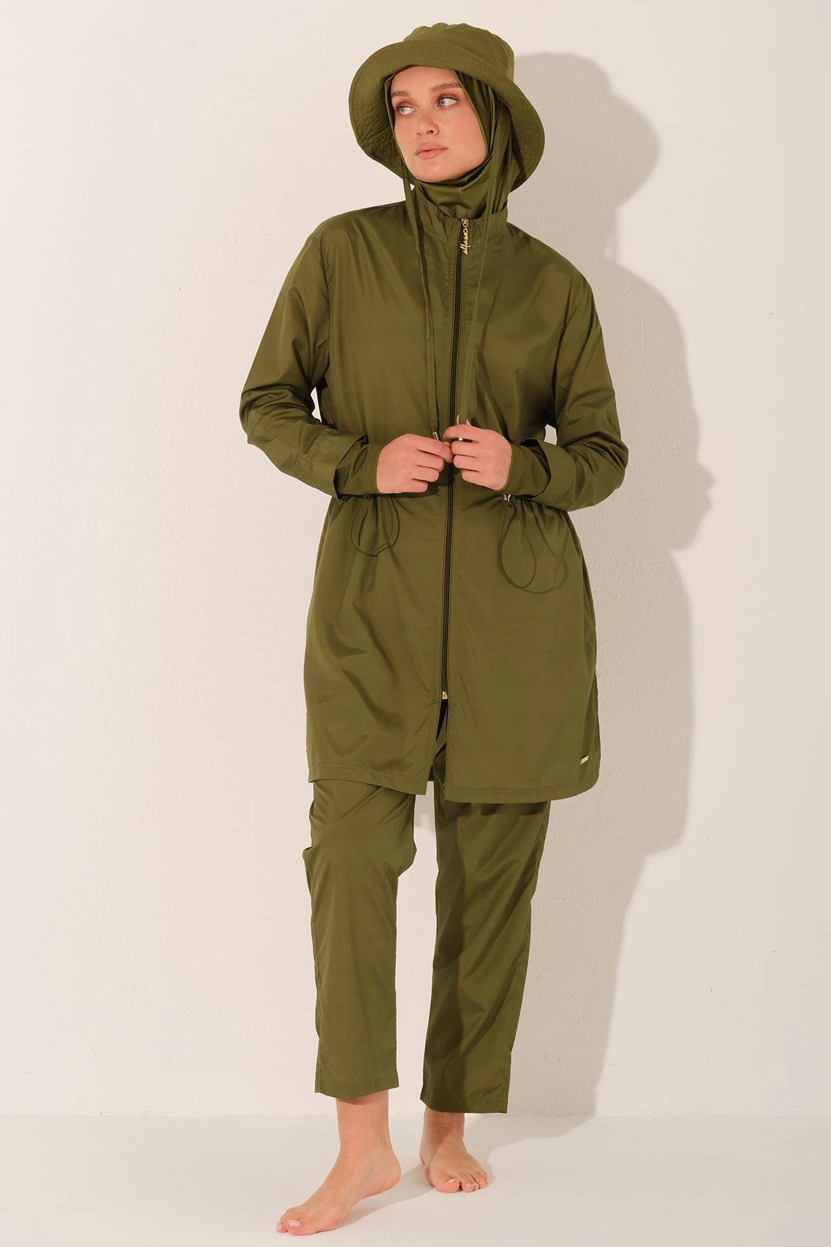 Woman in olive green burkini adjusting front zipper, full body shot.