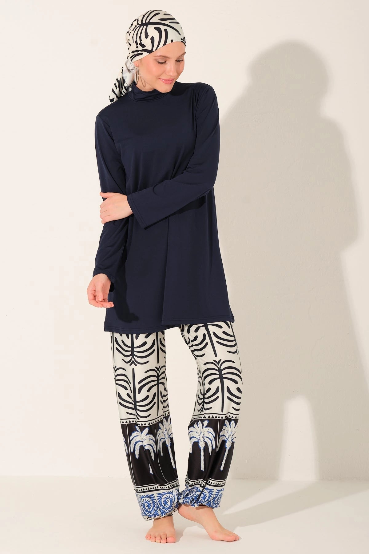 Woman in navy burkini set with patterned pants and scarf, arms crossed.